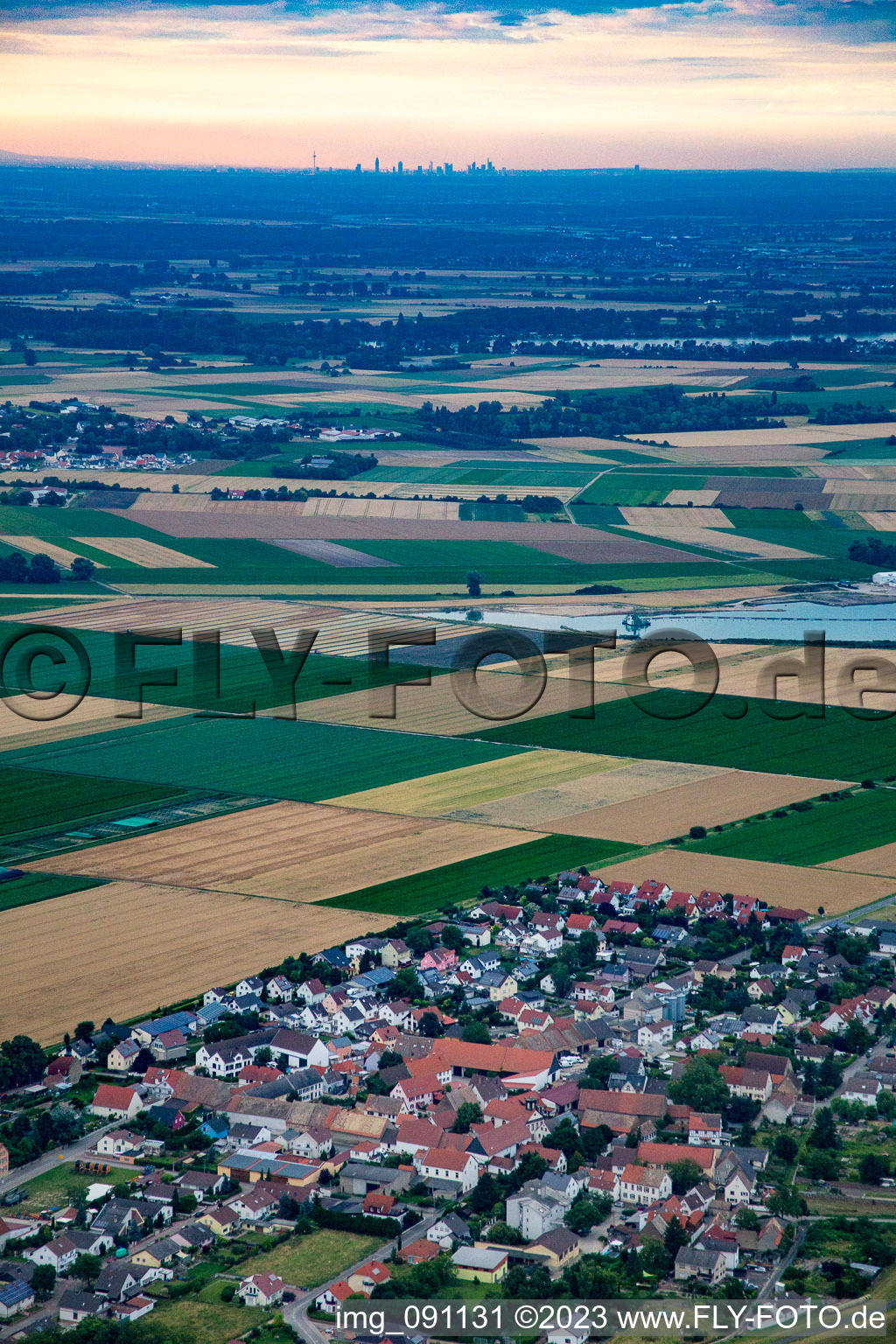Dorf - Ansicht am Rande von Feldern im Ortsteil Ibersheim in Worms vor der Skyline von Frankfurt am Main am Horizont im Bundesland Rheinland-Pfalz, Deutschland
