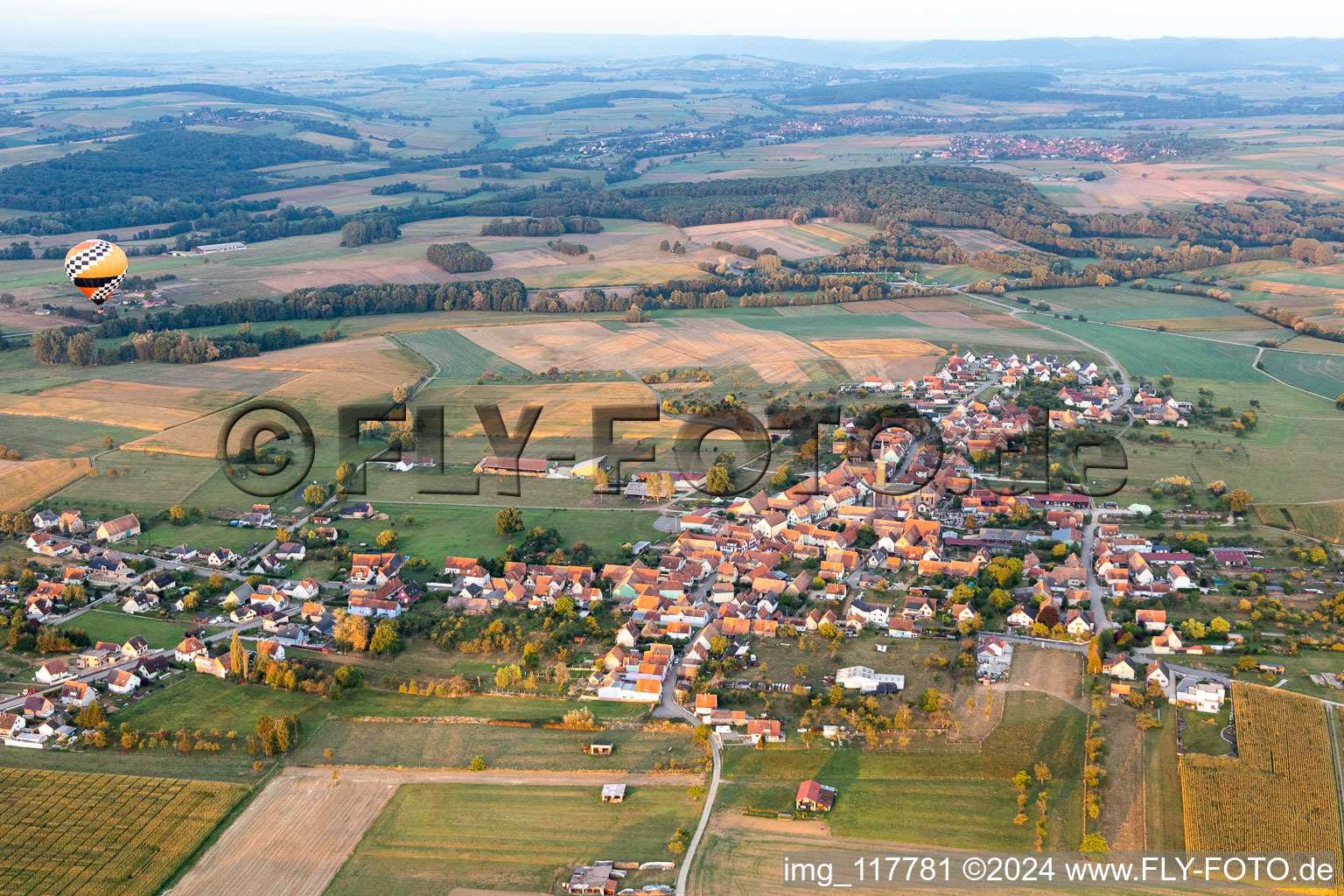 Landwirtschaftliche Nutzflächen und Feldgrenzen umsäumen das Siedlungsgebiet des Dorfes mit Heissluftballon in Kindwiller in Grand Est im Bundesland Bas-Rhin, Frankreich