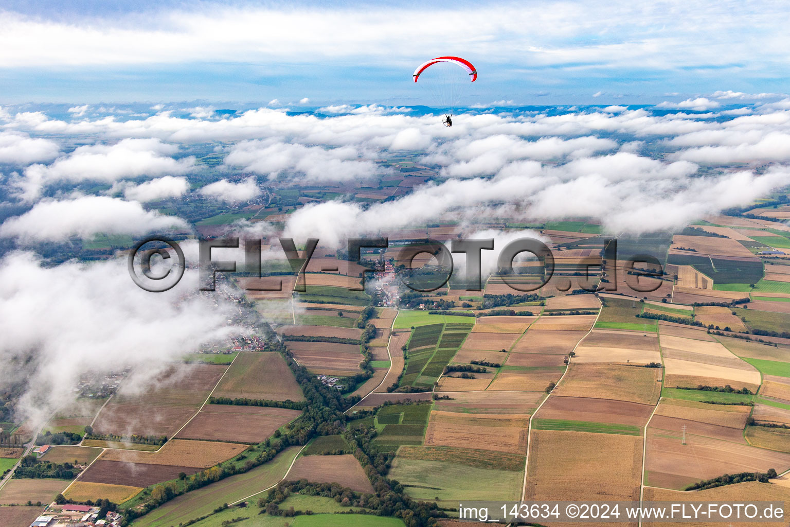 Paragleiter über dem Dorf in Wolken in Vollmersweiler im Bundesland Rheinland-Pfalz, Deutschland