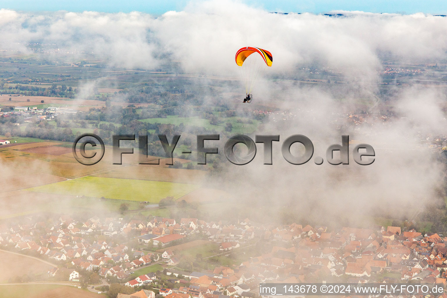 Luftbild von Ortschaft mit Gleitschirm unter herbstlichen Wolken in Steinweiler im Bundesland Rheinland-Pfalz, Deutschland