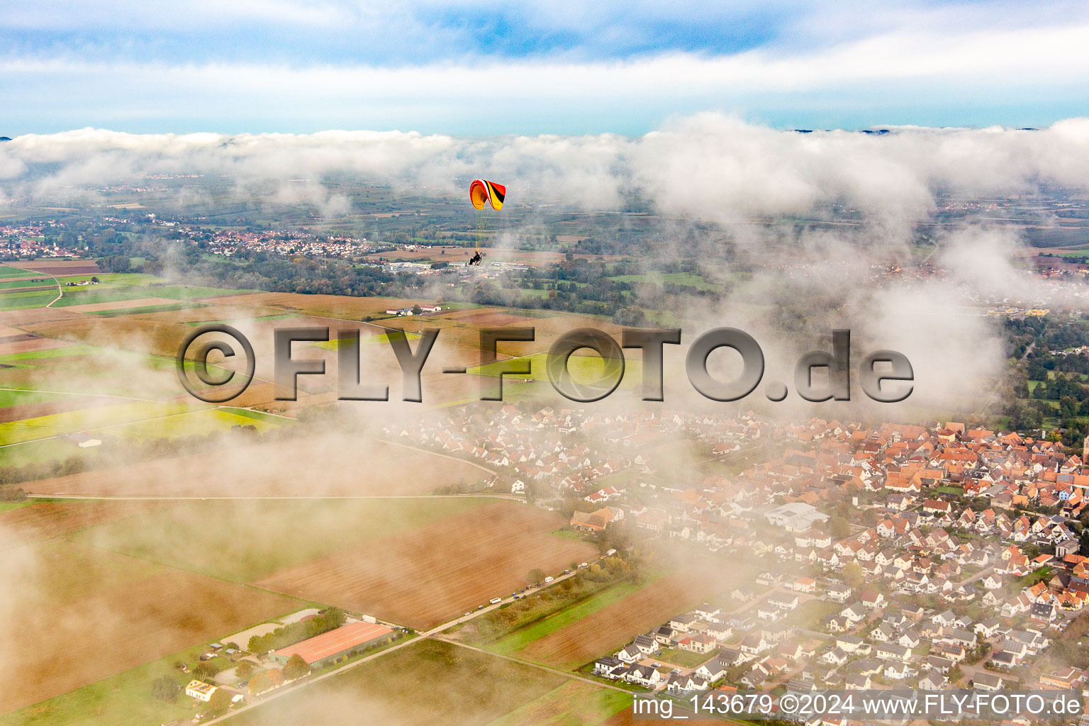 Luftaufnahme von Ortschaft mit Gleitschirm unter herbstlichen Wolken in Steinweiler im Bundesland Rheinland-Pfalz, Deutschland