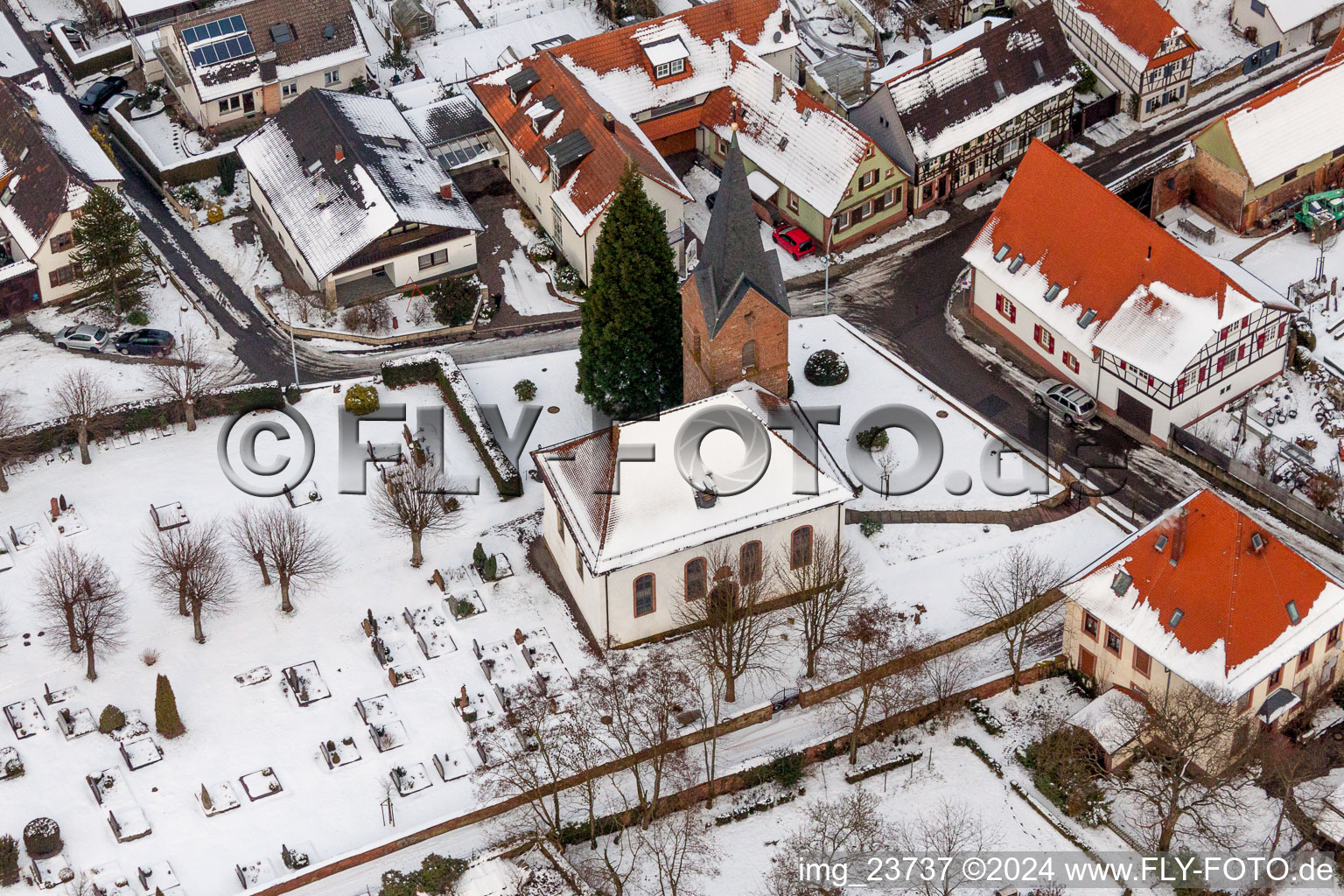 Winterlich schneebedeckte Kirchengebäude und Friedhof im Dorfkern in Winden im Bundesland Rheinland-Pfalz, Deutschland