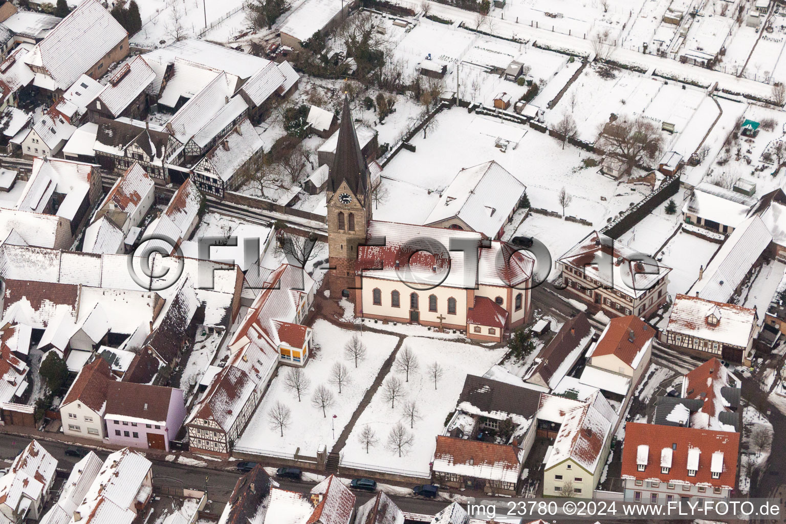 Winterlich schneebedeckte Kirchengebäude der katholischen Kirche in der Dorfmitte in Steinweiler im Bundesland Rheinland-Pfalz, Deutschland