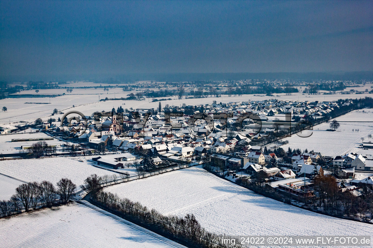 Winterlich schneebedeckte Dorf - Ansicht am Rande von landwirtschaftlichen Feldern und Nutzflächen in Neupotz im Bundesland Rheinland-Pfalz, Deutschland