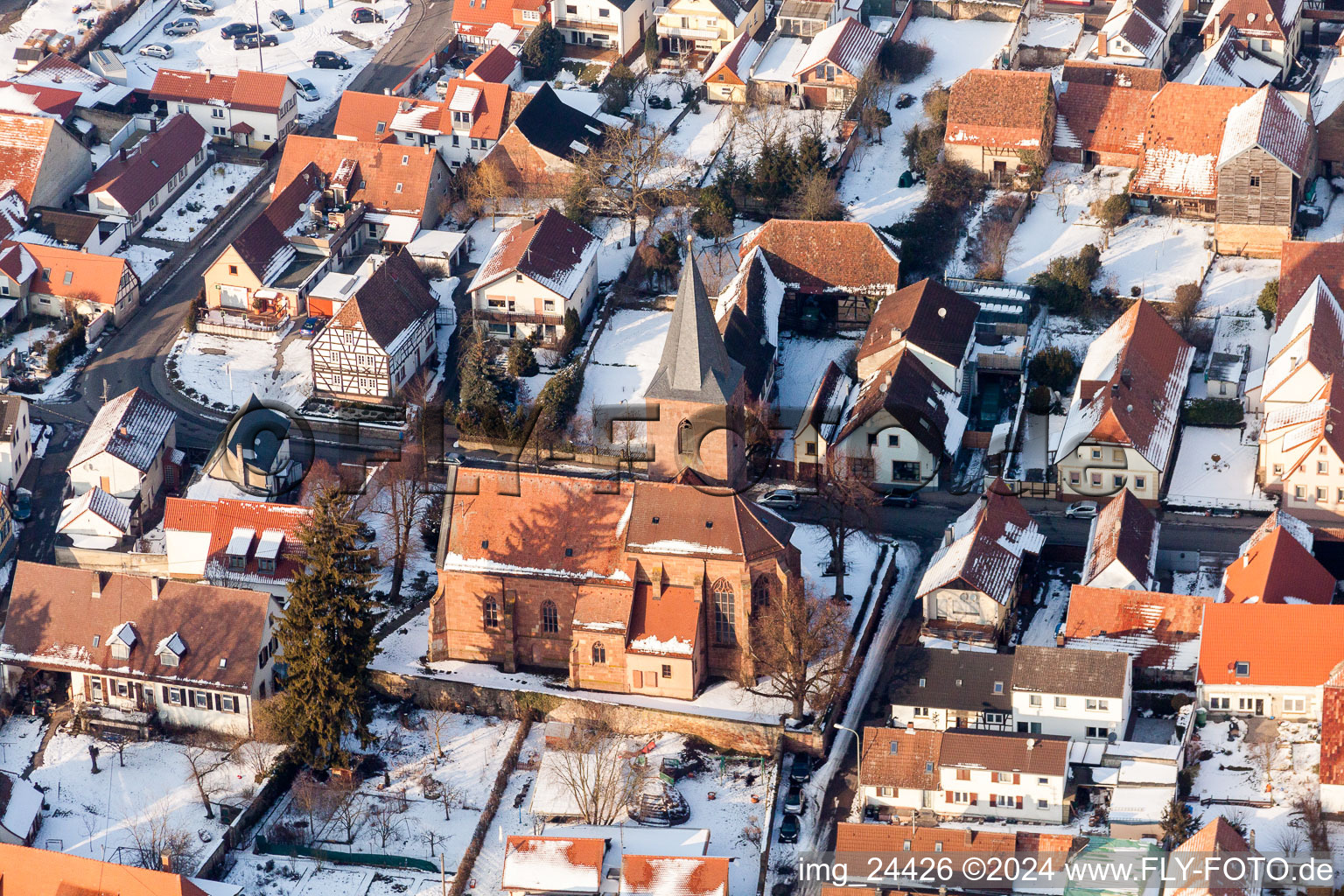 Winterlich schneebedeckte Kirchengebäude im Dorfkern in Rohrbach im Bundesland Rheinland-Pfalz, Deutschland