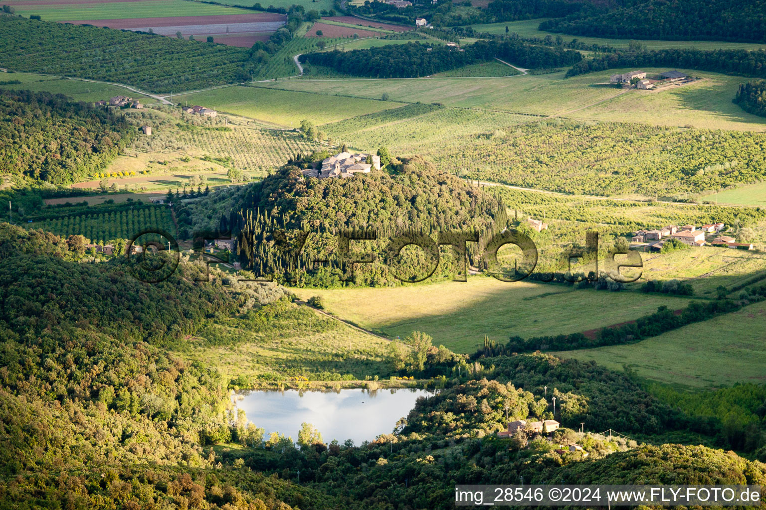 Dorf - Ansicht von Poggio Santa Cecilia auf einem bewaldeten, runden Hügel mit See in Toscana, Italien