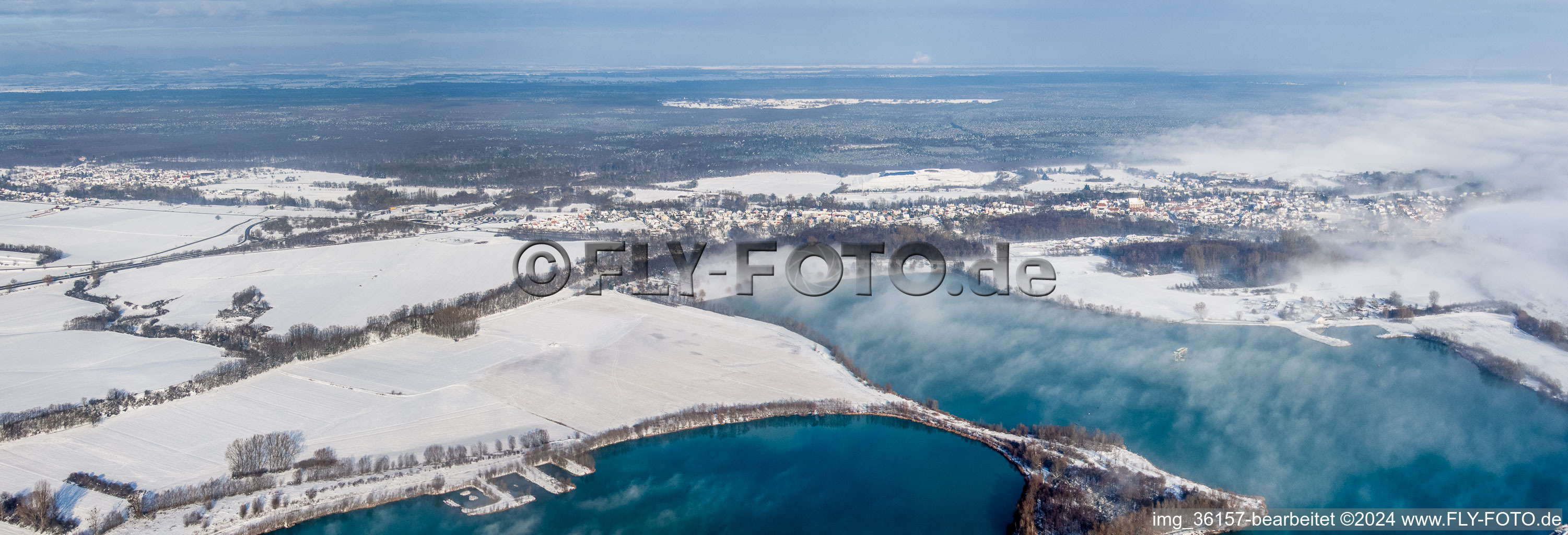 Panorama Perspektive Winterlich schneebedeckte Ortsansicht der Straßen und Häuser der Wohngebiete hinter Baggerseen in Lauterbourg in Grand Est im Ortsteil Neulauterburg im Bundesland Bas-Rhin, Frankreich