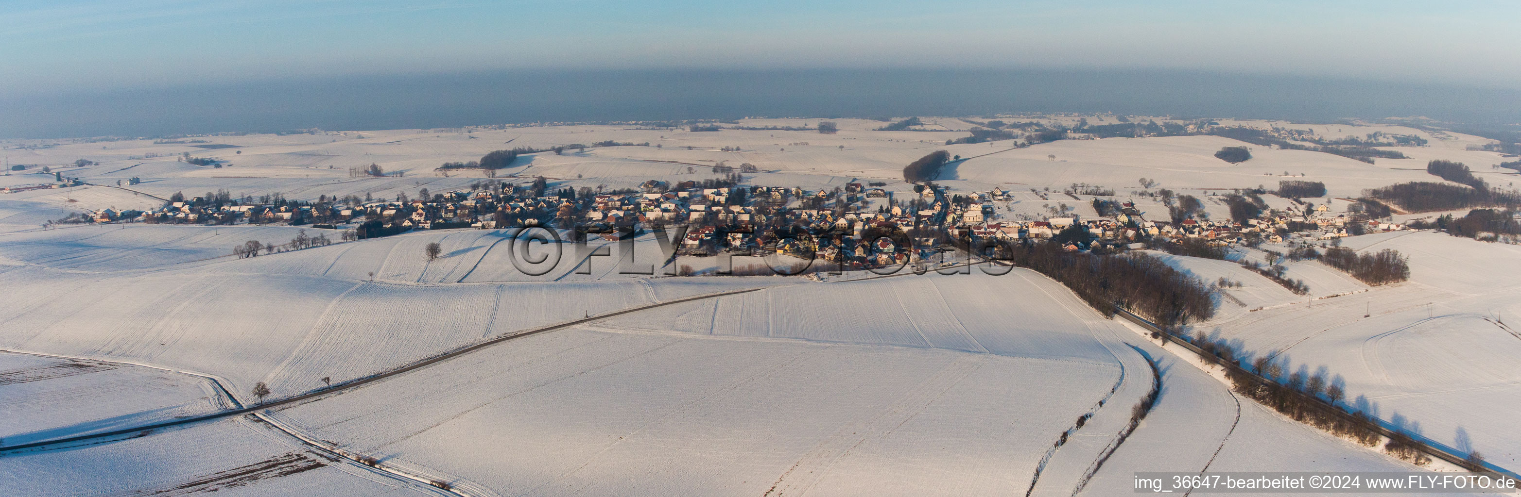 Panorama der winterlich schneebedeckten Dorf - Ansicht am Rande von landwirtschaftlichen Feldern und Nutzflächen in Wintzenbach in Grand Est im Bundesland Bas-Rhin, Frankreich