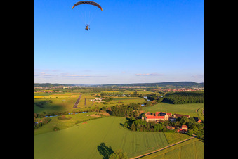 Paragleiter über dem Gut Mariaburghausen mit Kirche St. Johannes der Täufer Mariaburghausen in Haßfurt im Bundesland Bayern, Deutschland