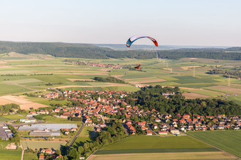 Paragleiter über einem Dorf am Rande von landwirtschaftlichen Feldern und Nutzflächen in Rüdenhausen im Bundesland Bayern, Deutschland