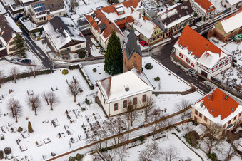 Winterlich schneebedeckte Kirchengebäude und Friedhof im Dorfkern in Winden im Bundesland Rheinland-Pfalz, Deutschland