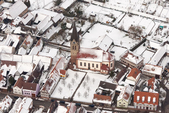 Winterlich schneebedeckte Kirchengebäude der katholischen Kirche in der Dorfmitte in Steinweiler im Bundesland Rheinland-Pfalz, Deutschland