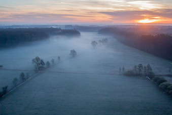 Morgennebel beim Sonnenaufgang über Grasflächen- Strukturen einer Feld- und Wiesen- Landschaft Otterbachtal in Minfeld im Bundesland Rheinland-Pfalz, Deutschland