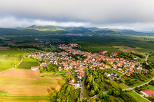 Dorf - Ansicht am Rande von landwirtschaftlichen Feldern und Nutzflächen im Morgenlicht vor tiefen Wolken in Göcklingen im Bundesland Rheinland-Pfalz, Deutschland